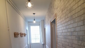 A narrow hallway with a checkered floor, white walls, and a brick wall on one side. There is a radiator on the left and a door on the right. - Le Paradis near Beauval. (Orbigny)
