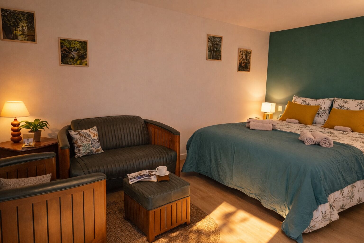 A hotel room with a bed, a sofa, a small table with a lamp, and a potted plant.