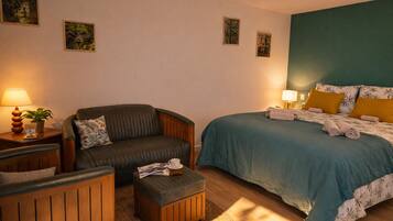 A hotel room with a bed, a sofa, a small table with a lamp, and a potted plant.