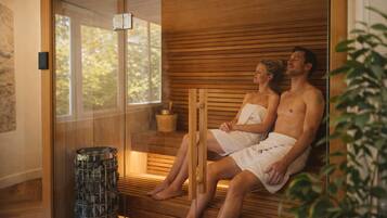 A sauna with wooden benches, a glass door, and a stone container.
