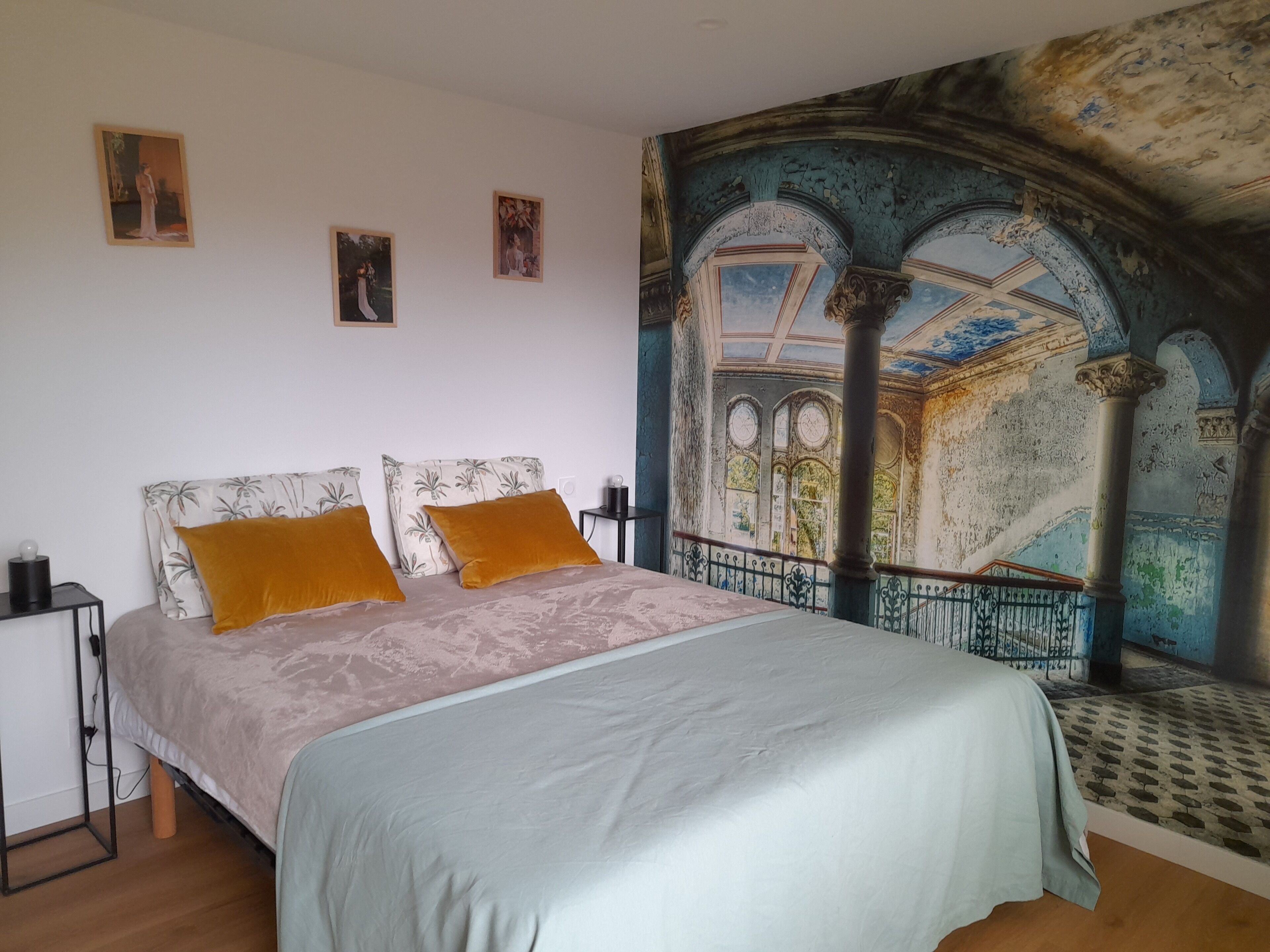 A bedroom with a bed, two pillows, a nightstand, and a wall mural.