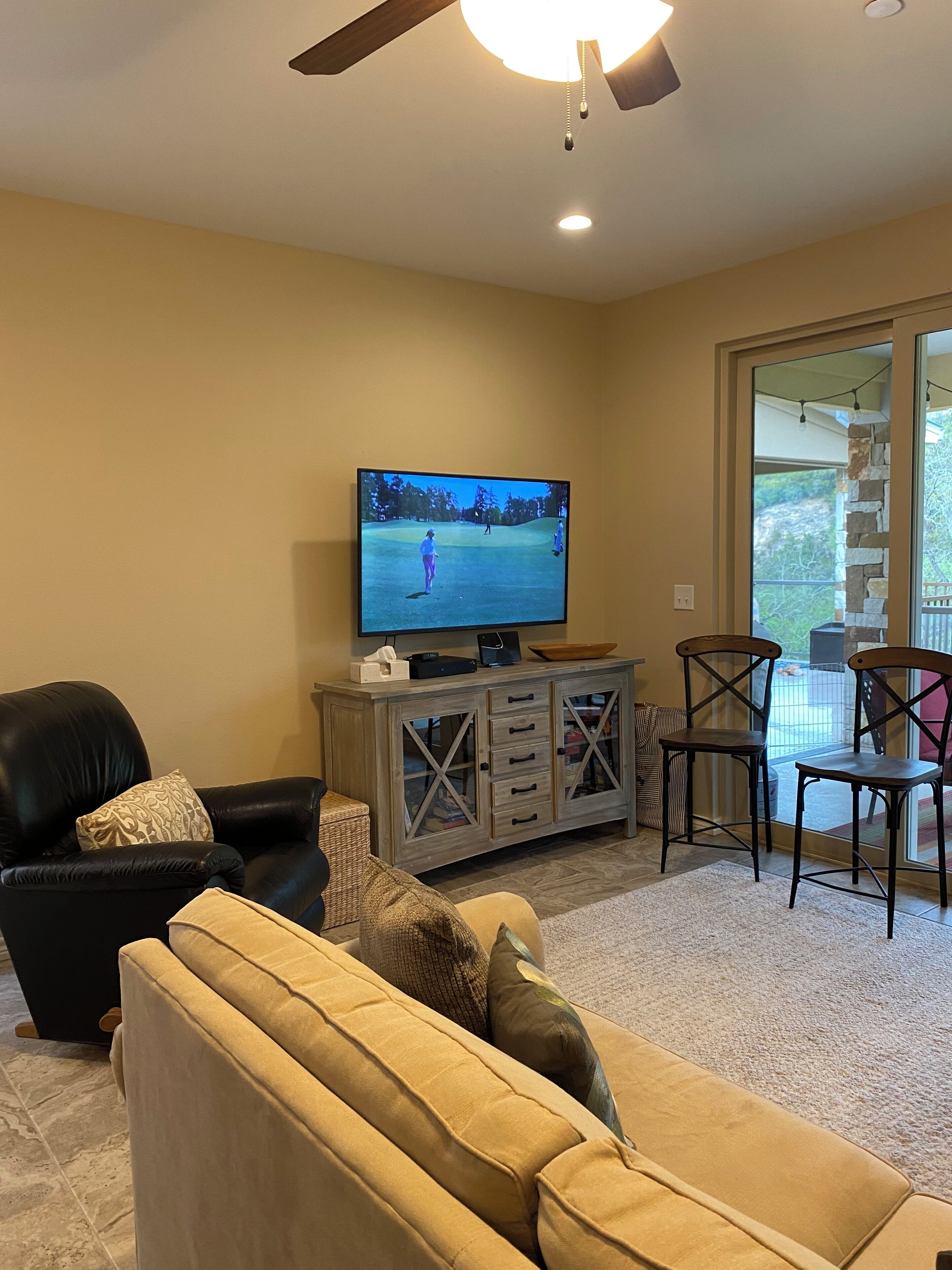 A living room with a television, a black leather chair, a beige sofa, and a wooden cabinet.