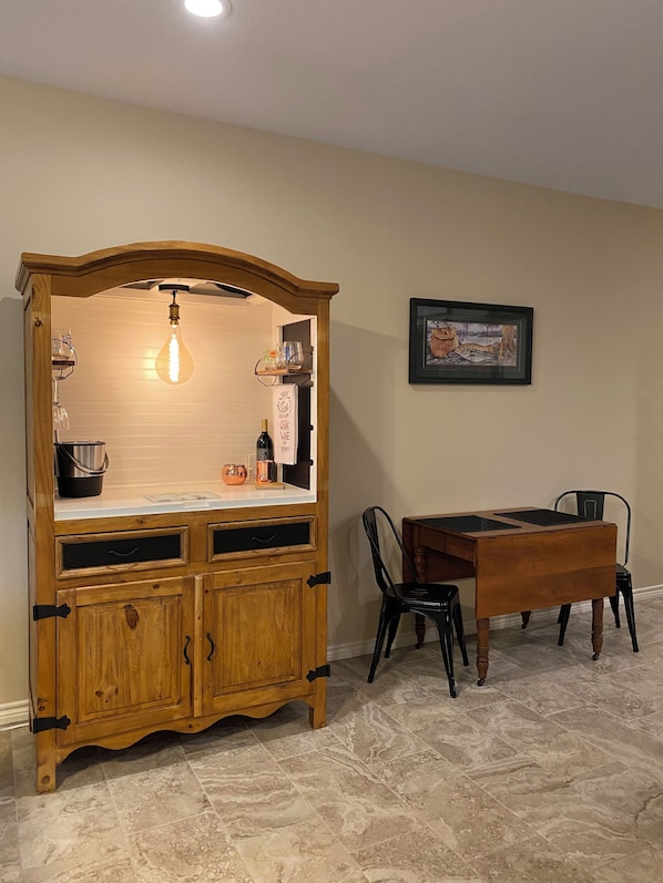 A wooden cabinet with a light bulb hanging above, a framed picture on the wall, and a dining table with chairs. - On River Time...Cozy 3-br 2-ba condo in gated complex, pool, direct river access (New Braunfels)