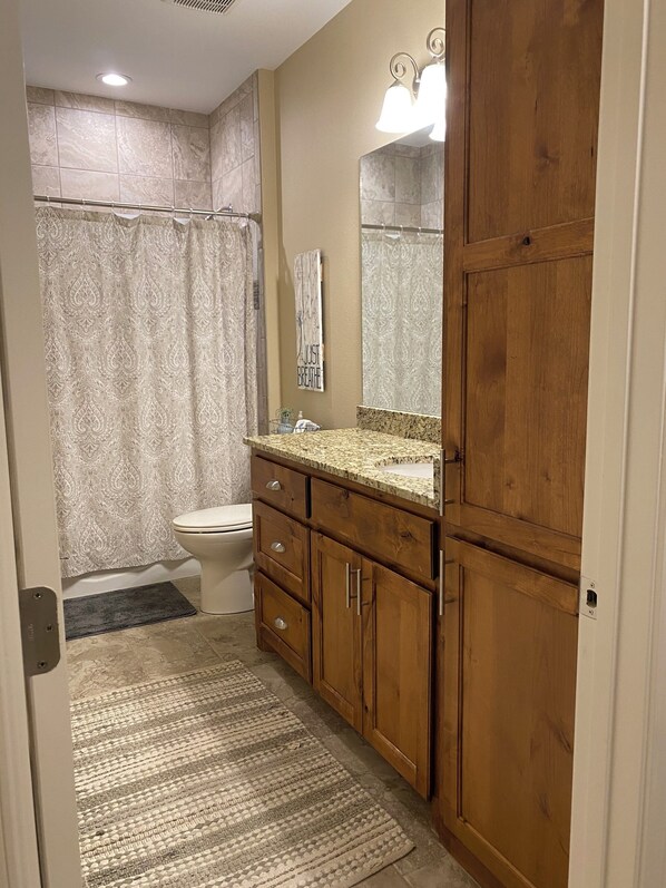 A bathroom with a toilet, vanity with a mirror, wooden cabinets, and a shower curtain.