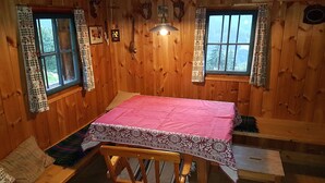 A wooden cabin room with a bed, a table, and two windows with curtains. - Hut for skiing or hiking (Pill)
