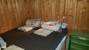 A room with a bed, pillows, and a green storage unit. - Hut for skiing or hiking (Pill)