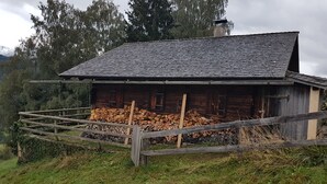 A rustic wooden cabin with a sloped roof, surrounded by a wooden fence and a stack of firewood. - Hut for skiing or hiking (Pill)