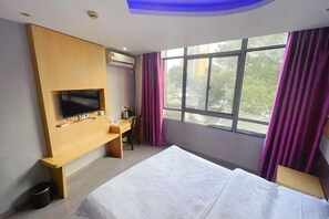 Una habitación de hotel con cama, escritorio, televisor y ventana con cortinas.