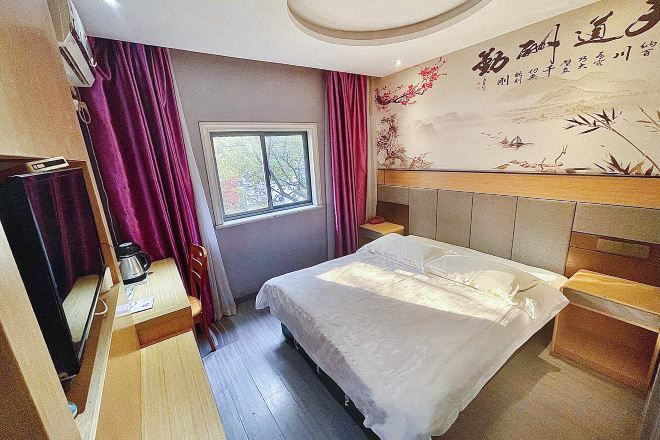 Quarto de hotel com cama, escrivaninha, cadeira, janela e parede com um desenho decorativo.