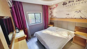 Quarto de hotel com cama, escrivaninha, cadeira, janela e parede com um desenho decorativo.