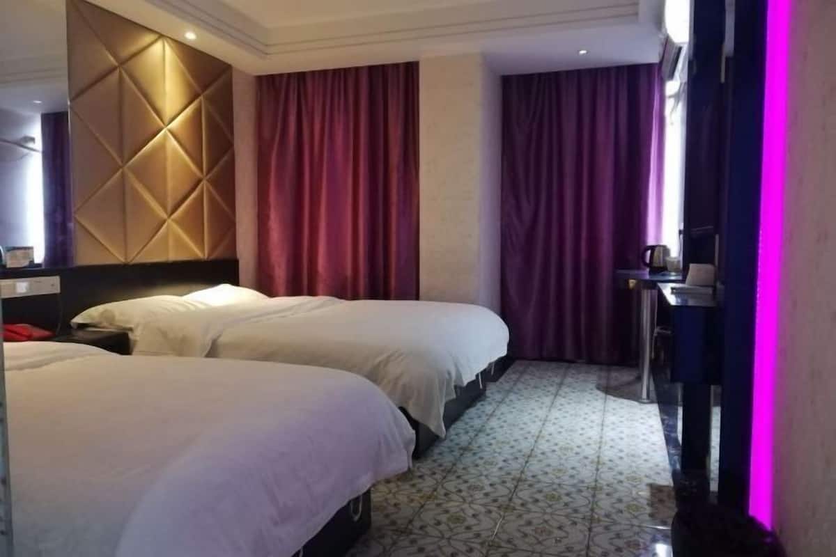 Une chambre d’hôtel avec deux lits, un bureau, une chaise et une grande fenêtre avec des rideaux.