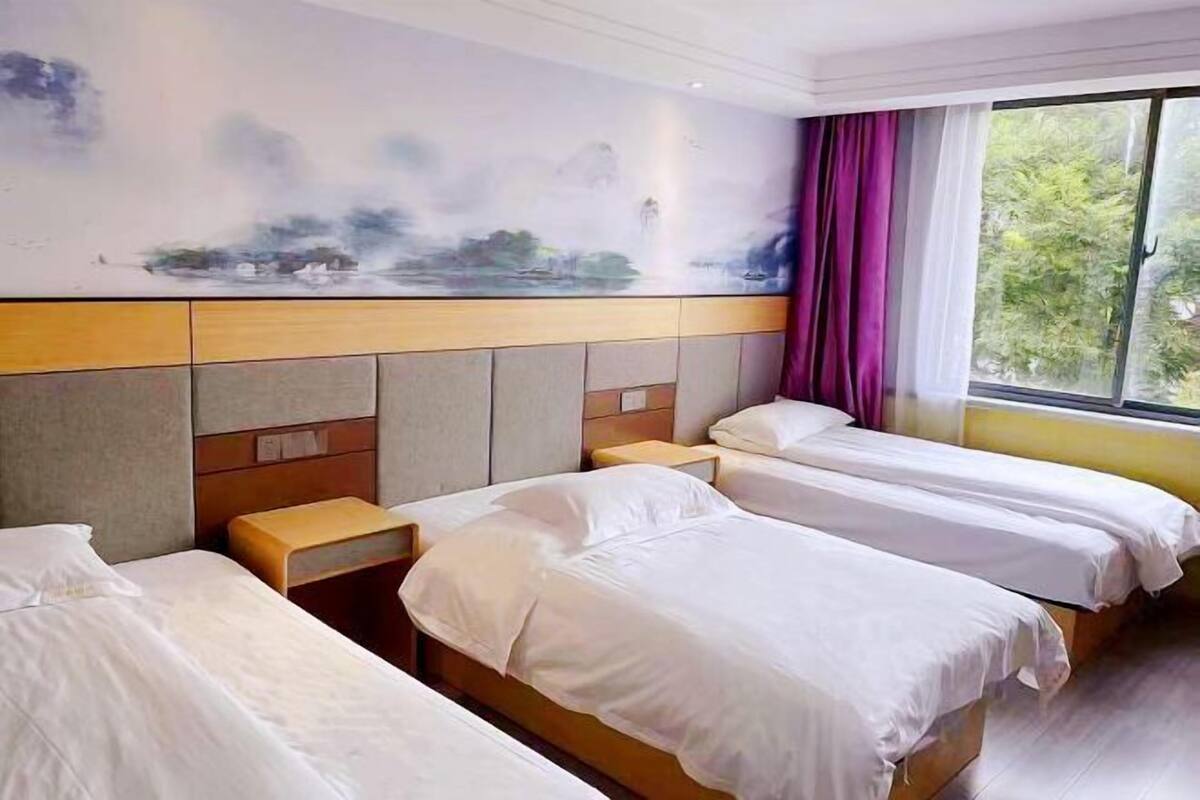 Une chambre d’hôtel avec trois lits simples, une grande fenêtre avec des rideaux et une fresque murale.