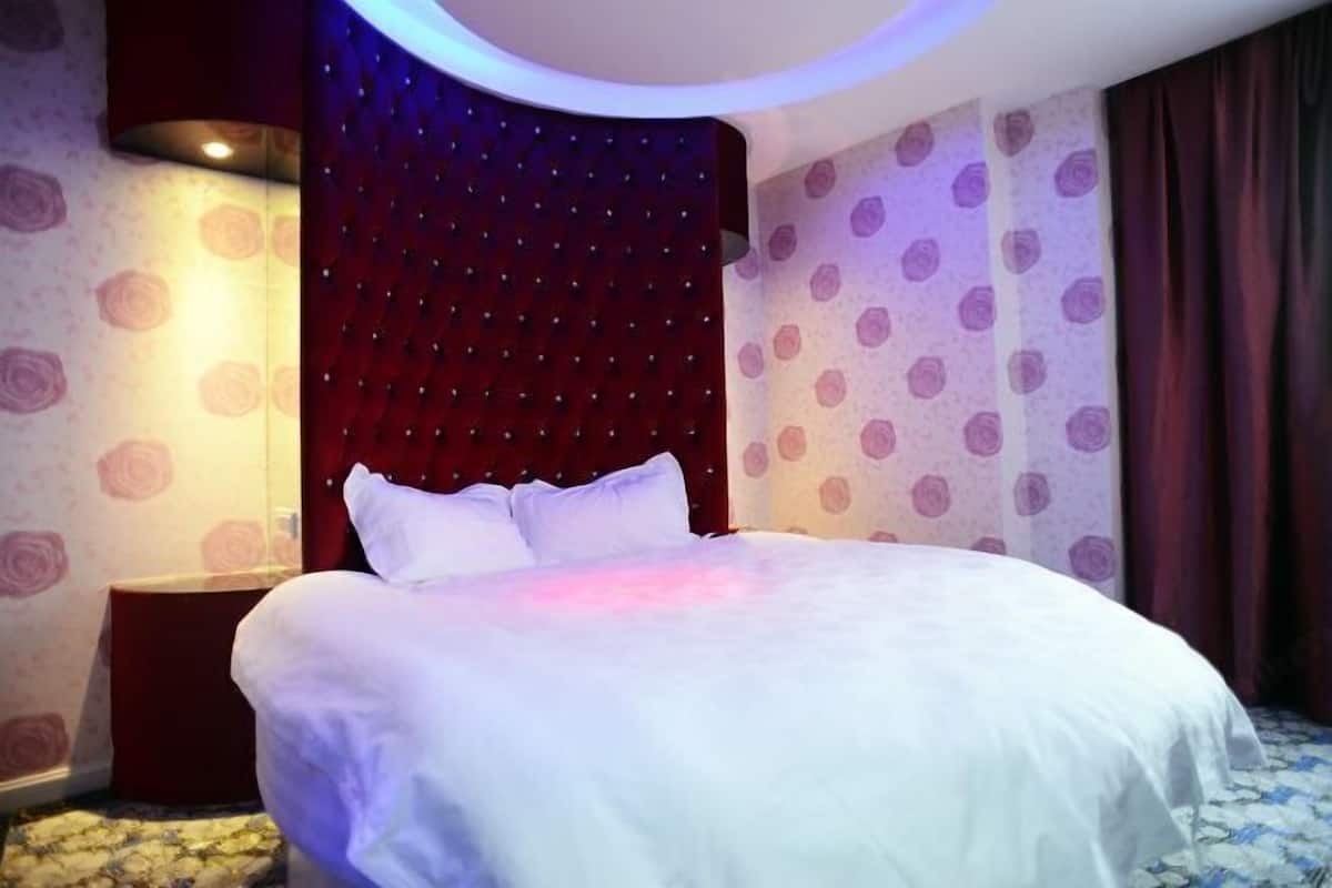 Une chambre d’hôtel avec un grand lit, une tête de lit à motifs capitonnés, une table de chevet et un mur décoré d’un motif.