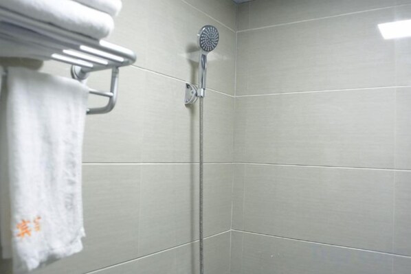 Une douche équipée d’un pommeau de douche à main, un porte-serviettes avec une serviette pliée, et des murs carrelés.