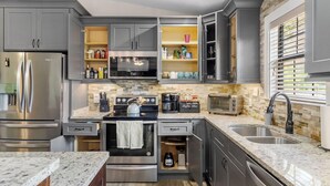 Une cuisine moderne avec des meubles gris, des appareils en acier inoxydable, un plan de travail en granit et un pare-feu en pierre.