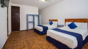 Habitación de hotel con dos camas, ventilador de techo, piso de madera y una mesita de noche.