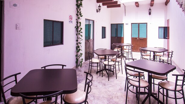 Un área de comedor con varias mesas y sillas, una escalera y una puerta con un cartel de 'No Smoking'.