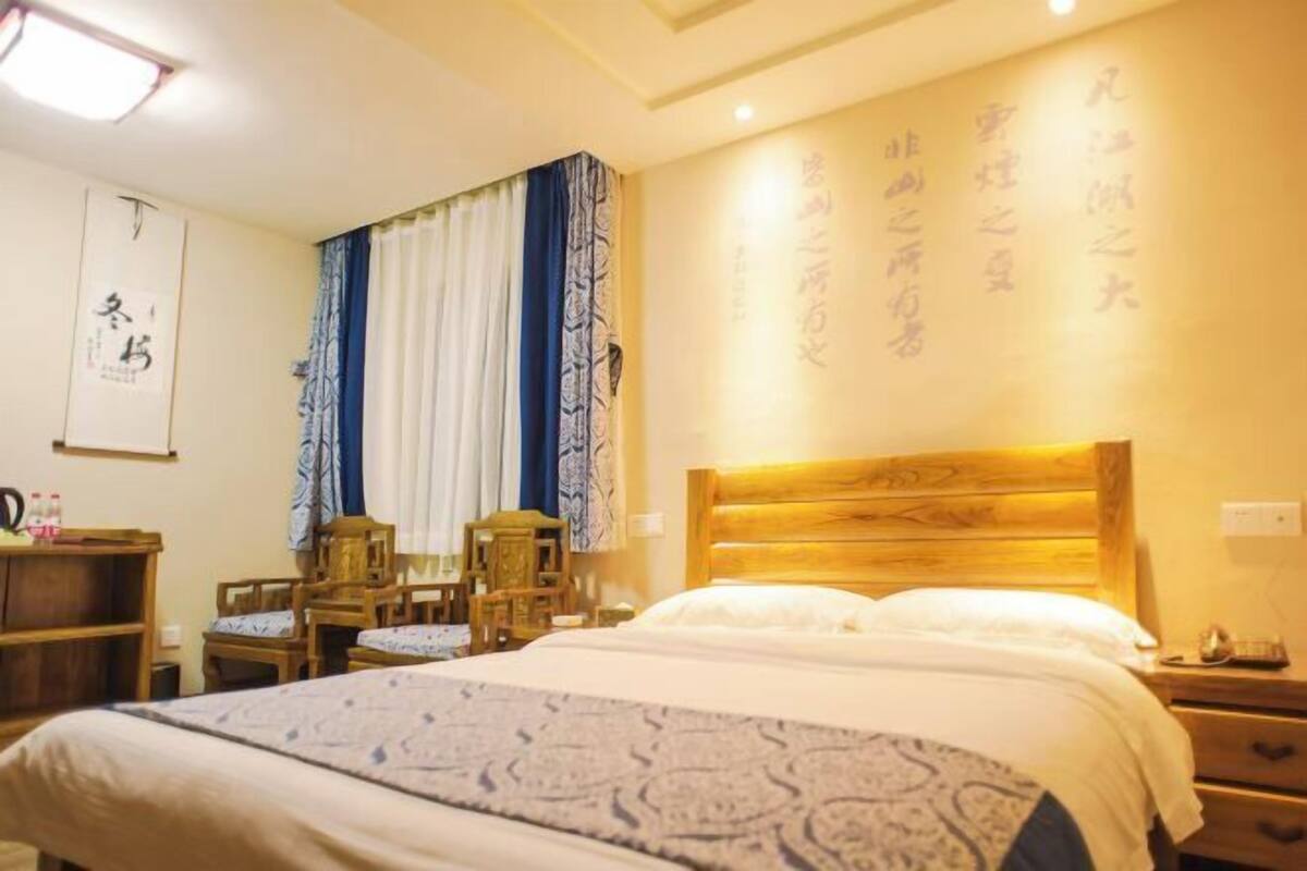 A hotel room with a bed, wooden headboard, bedside tables, a desk, chairs, and a curtain.