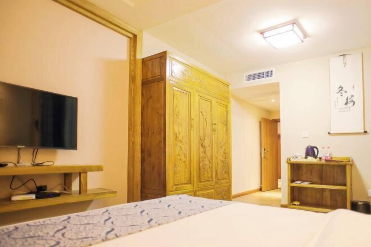 A hotel room with a bed, a television on a stand, a wardrobe, and a shelf with items.