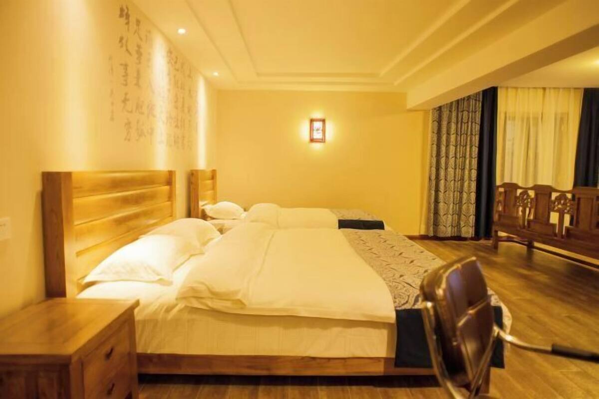 A hotel room with a wooden bed, a nightstand, a chair, and a wall with calligraphy.