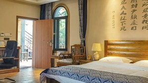 Quarto de hotel com cama, escrivaninha, cadeira, abajur e janela com cortinas.