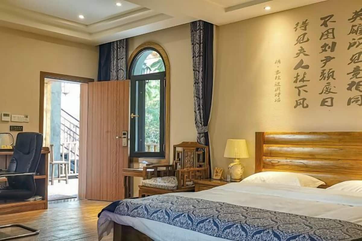 A hotel room with a bed, a desk, a chair, a lamp, and a window with curtains.
