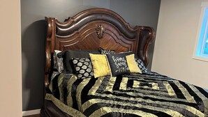 A bed with a dark wooden headboard, a black and gold patterned bedspread, and several pillows including one with "home sweet home" text. - Cozy Creekside Cottage (Hope)