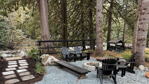 A forested campsite with a gravel path leading to seating areas with Adirondack chairs and a wooden bench. - Cozy Creekside Cottage (Hope)