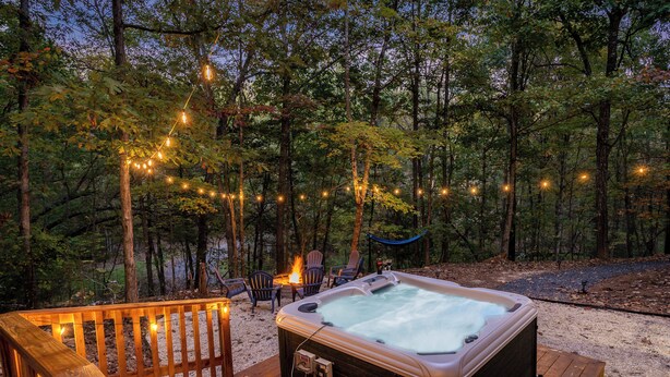 Un bain à remous situé dans un espace boisé, agrémenté de guirlandes lumineuses et de chaises.