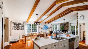 Une cuisine spacieuse avec des poutres en bois, un grand îlot central et un mur d’accent en pierre.