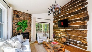 Un salon avec un mur en pierre, une cheminée, un canapé, une table basse et un téléviseur fixé à un mur en bois.