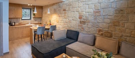 A modern living room with a stone wall, a sofa, a dining area, and a kitchen.