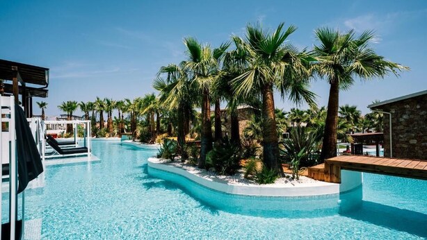 A swimming pool with palm trees, a stone building, and a covered area. - Kallithea Village (Kassandra)