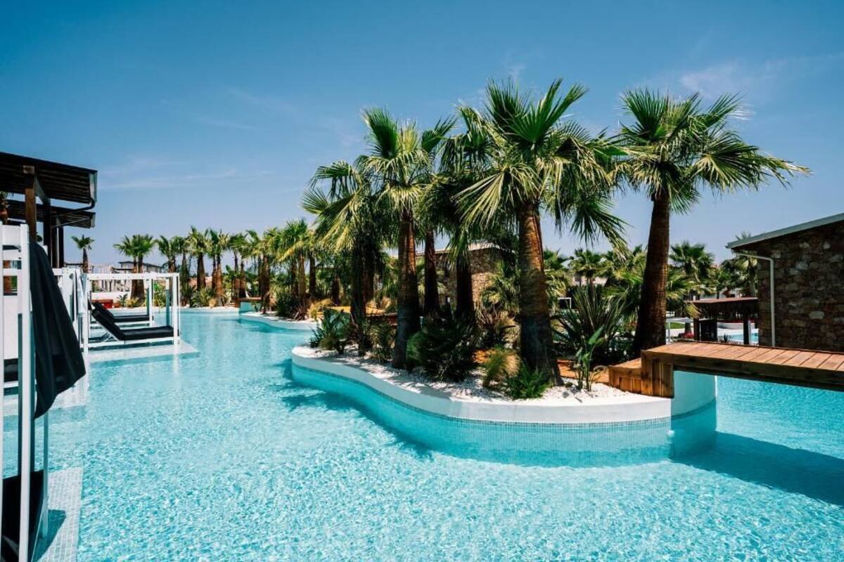 Una piscina con palmeras, un edificio de piedra y una zona techada.