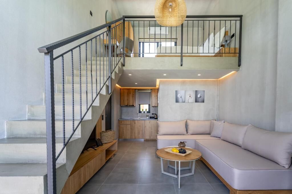 Un interior moderno con una escalera, una sala de estar con sofá y mesa de centro, y una cocina al fondo.