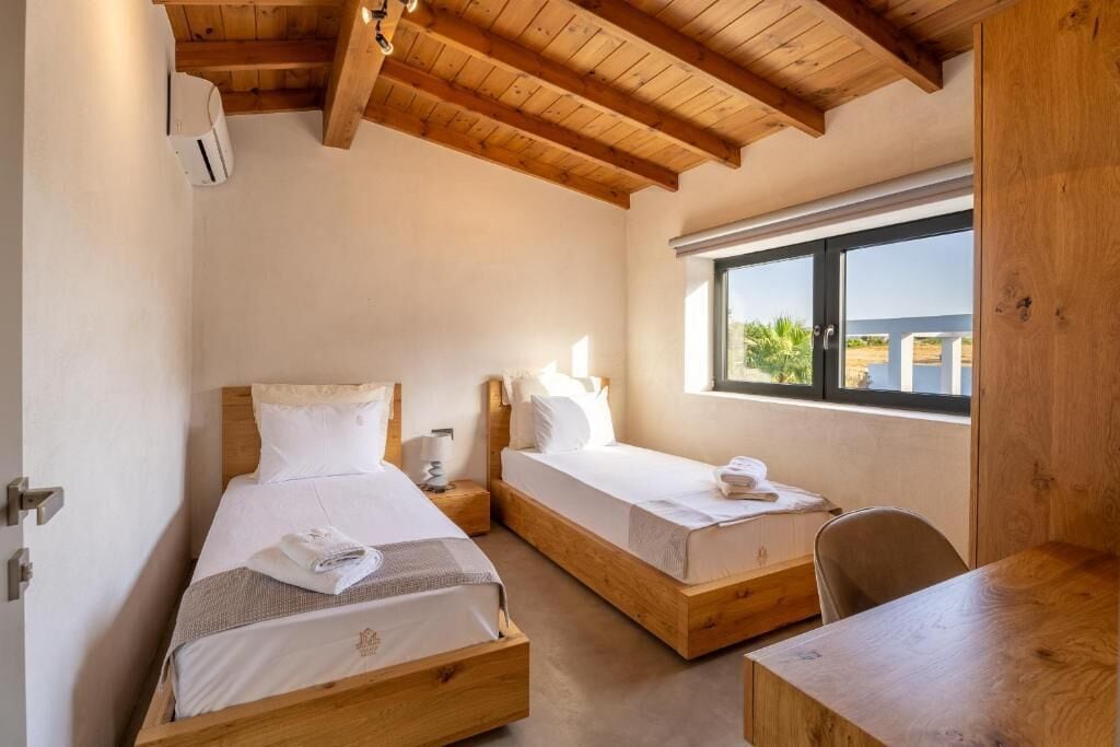 Un dormitorio con dos camas de madera, un escritorio de madera y una ventana con vistas al exterior.