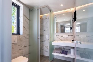 A modern bathroom with a toilet, a glass shower enclosure, and a marble wall. - Kallithea Village (Kassandra)