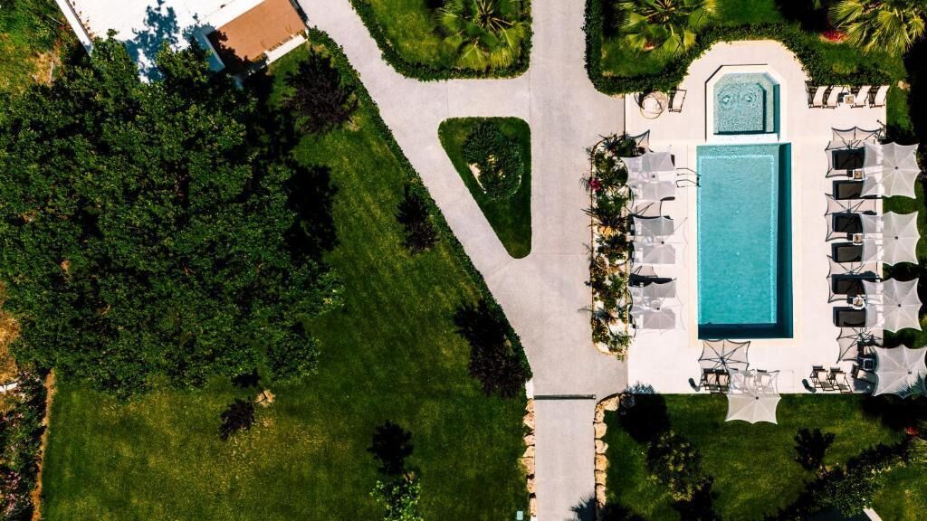 An aerial view of a resort with a swimming pool, lounge chairs, and a well-maintained lawn.