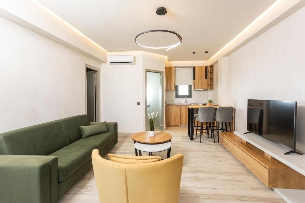 Ein modernes Wohnzimmer mit einem grünen Sofa, einem gelben Sessel, einem kleinen runden Tisch und einem Fernseher auf einer Holzkonsole.