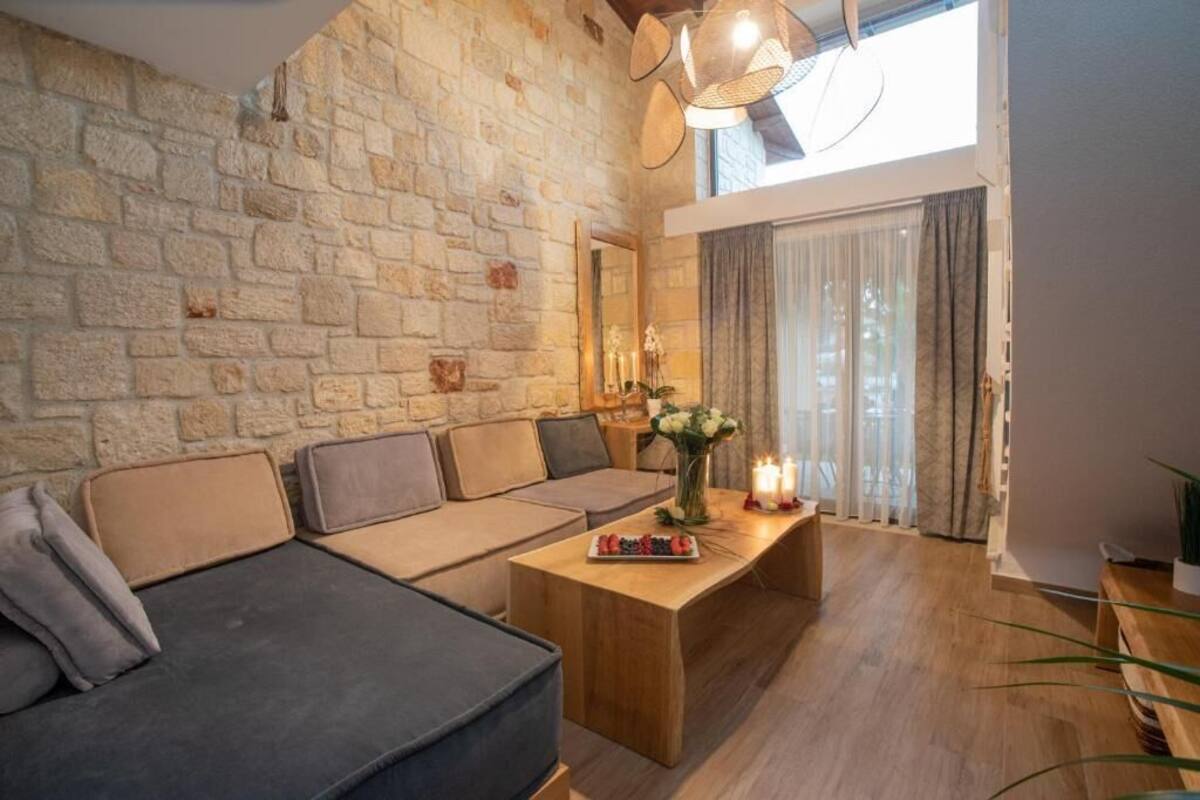 Un salón acogedor con pared de piedra, un conjunto de sofás, una mesa de centro de madera y un gran ventanal con cortinas.