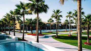 Un complex turístic amb piscina, palmeres i un edifici amb grans finestres.