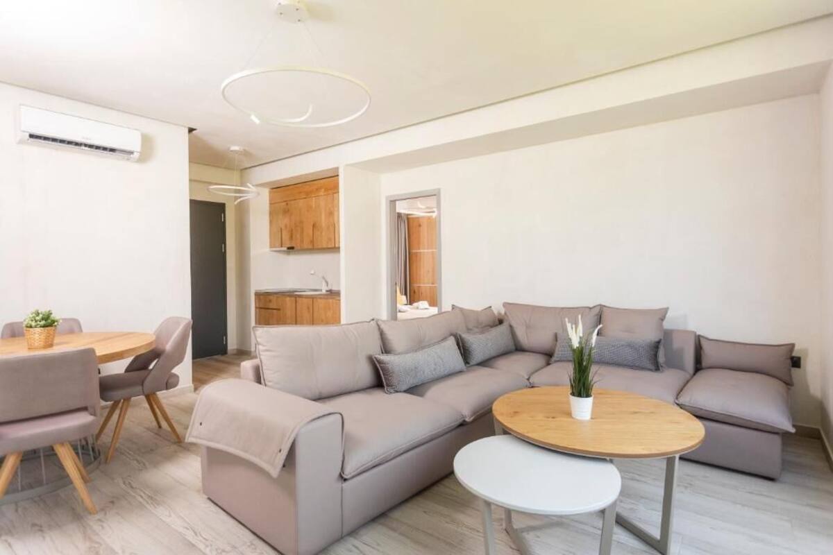 Una sala de estar moderna con un sofá color beige, una mesa de centro redonda de madera y un comedor con una mesa y sillas.