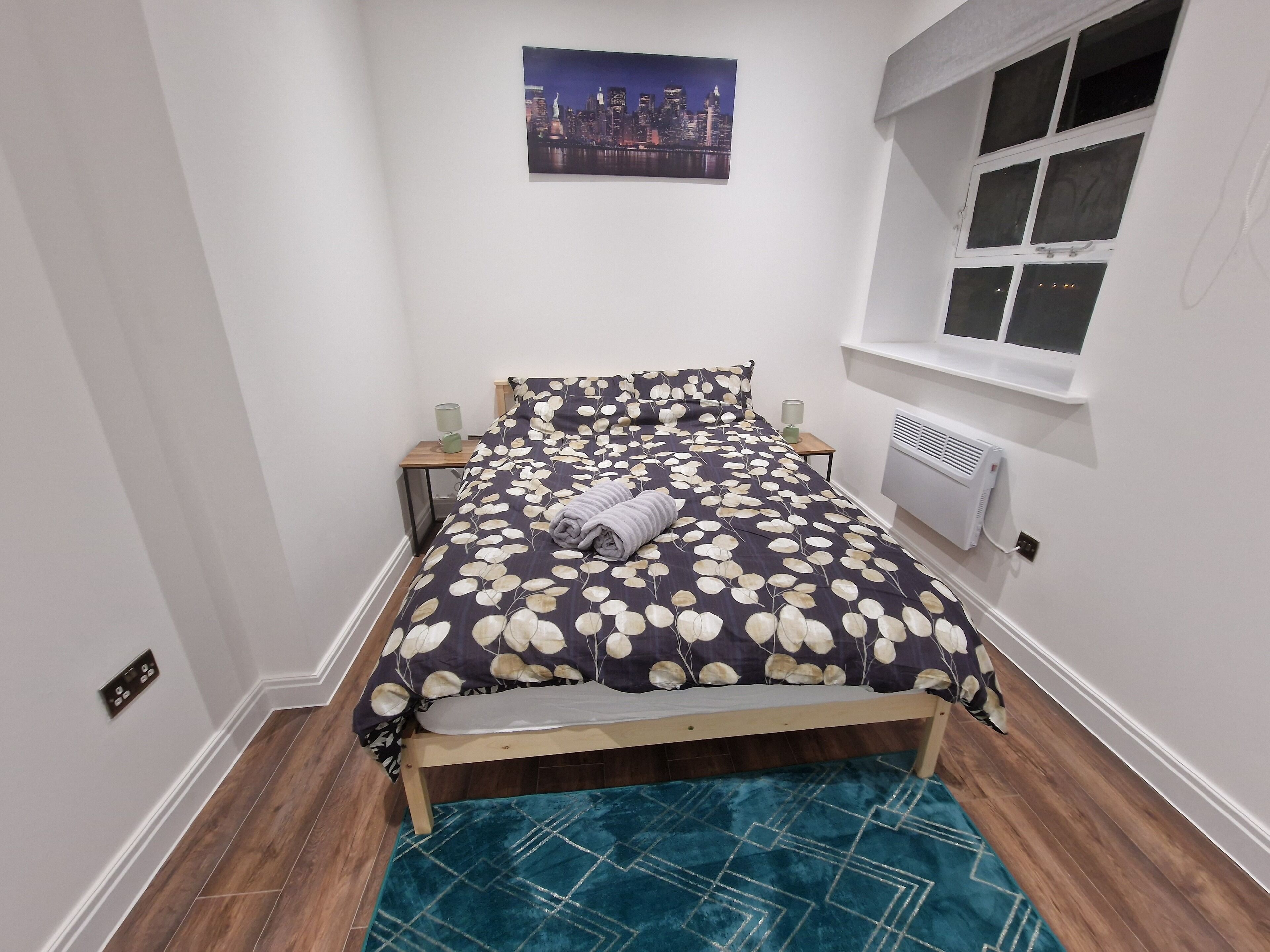 A bedroom with a bed, a nightstand, a lamp, a radiator, and a window.