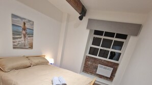 A bedroom with a bed, a painting, a window, and a brick wall. - Delightful New Period Conversion (Burnley)