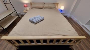 A neatly made bed with a beige bedspread and two pillows, a folded towel on the bed, and two bedside lamps on either side.