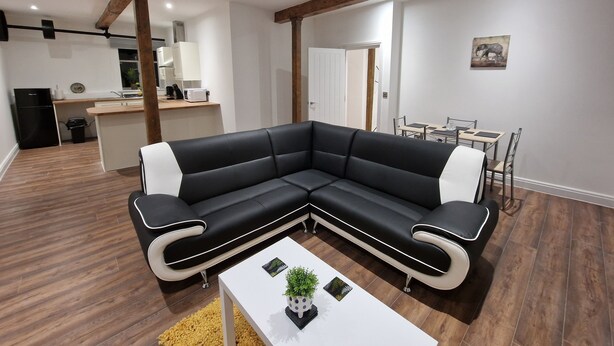 A modern living room with a black and white sectional sofa, a white coffee table, and a dining area with a table and chairs. - Delightful New Period Conversion (Burnley)