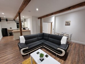 A modern living room with a black and white sectional sofa, a white coffee table, and a dining area with a table and chairs. - Delightful New Period Conversion (Burnley)