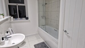 A modern bathroom with a white sink, a glass shower enclosure, and a door. - Delightful New Period Conversion (Burnley)