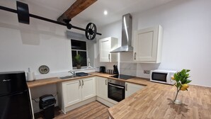 A modern kitchen with white cabinets, a wooden countertop, a built-in oven, and a stainless steel range hood. - Delightful New Period Conversion (Burnley)