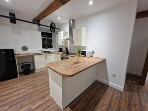 A modern kitchen with a wooden island, white cabinets, and a black refrigerator. - Delightful New Period Conversion (Burnley)